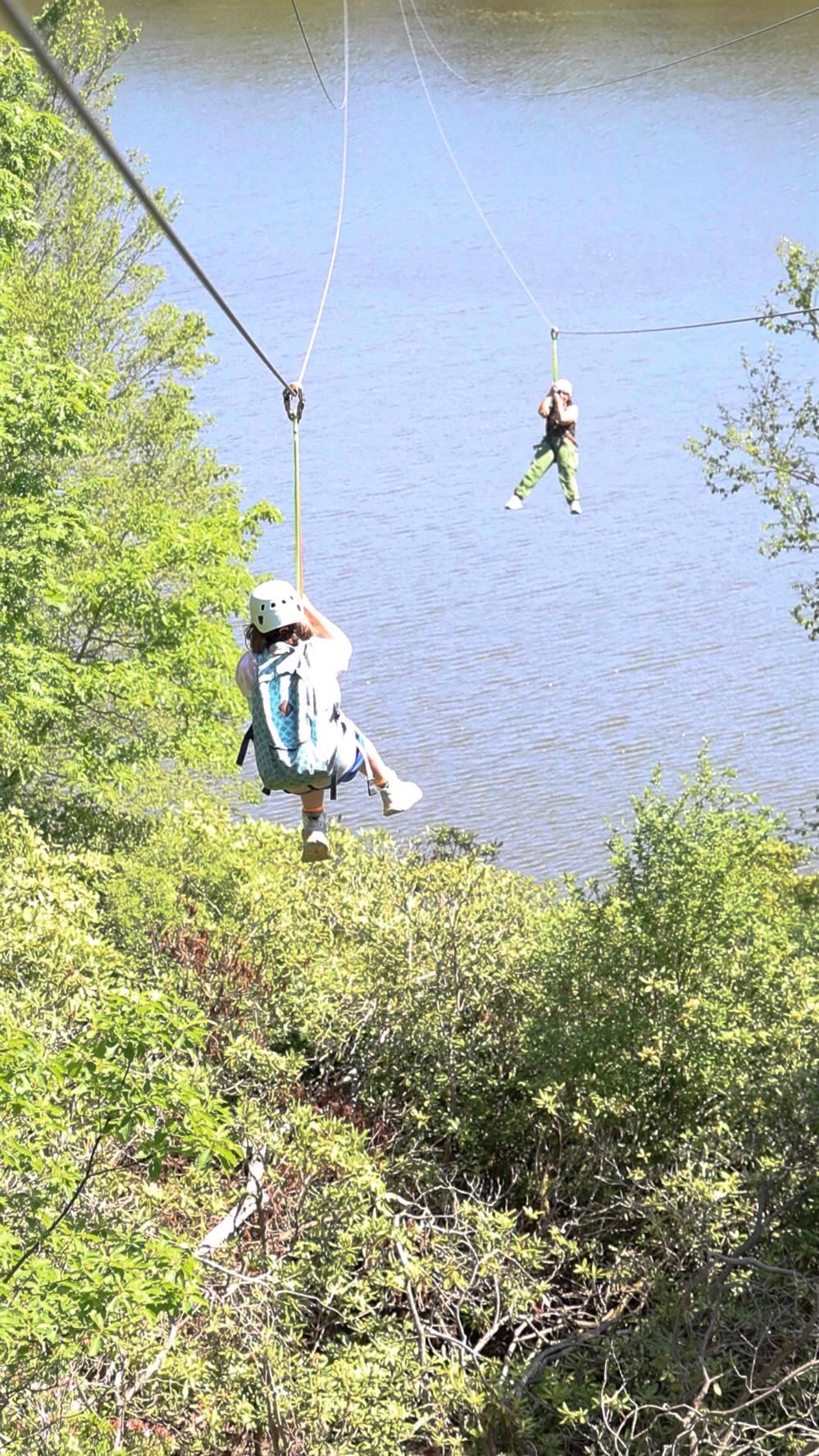  Two people are riding down a zip line over a lake